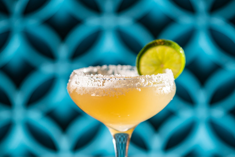 Salt-rimmed margarita garnished with a lime wheel against a bright turquoise background.