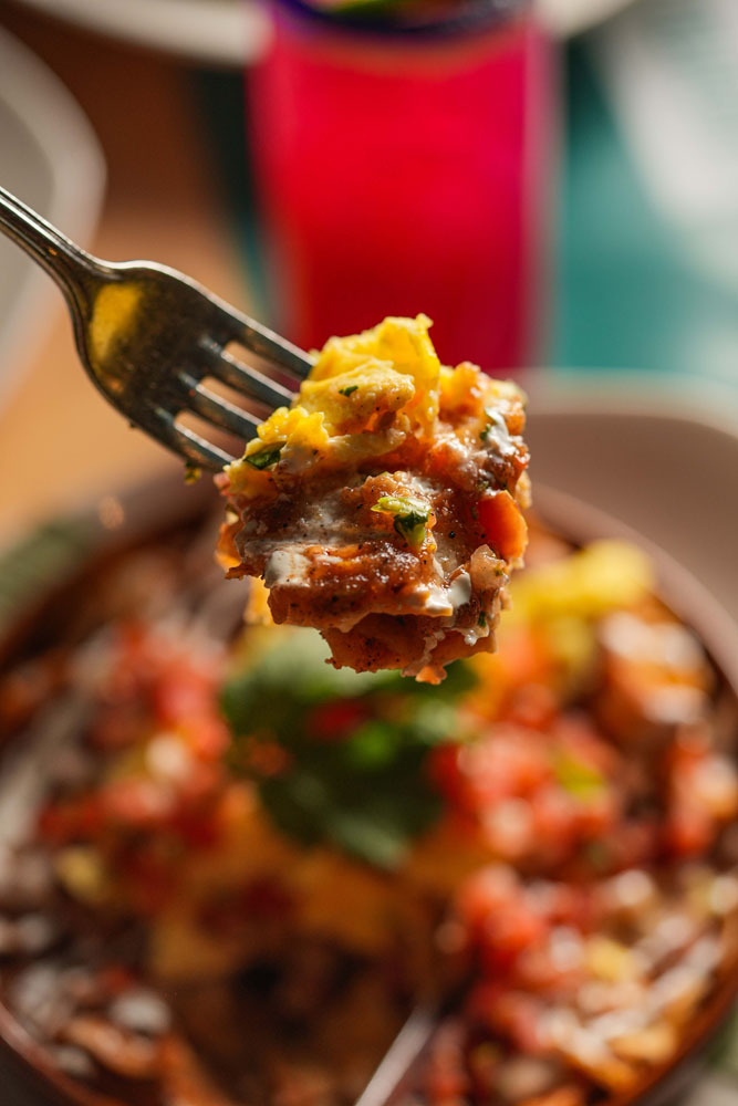 Forkful of a Mexican breakfast dish topped with eggs, salsa, and crema.