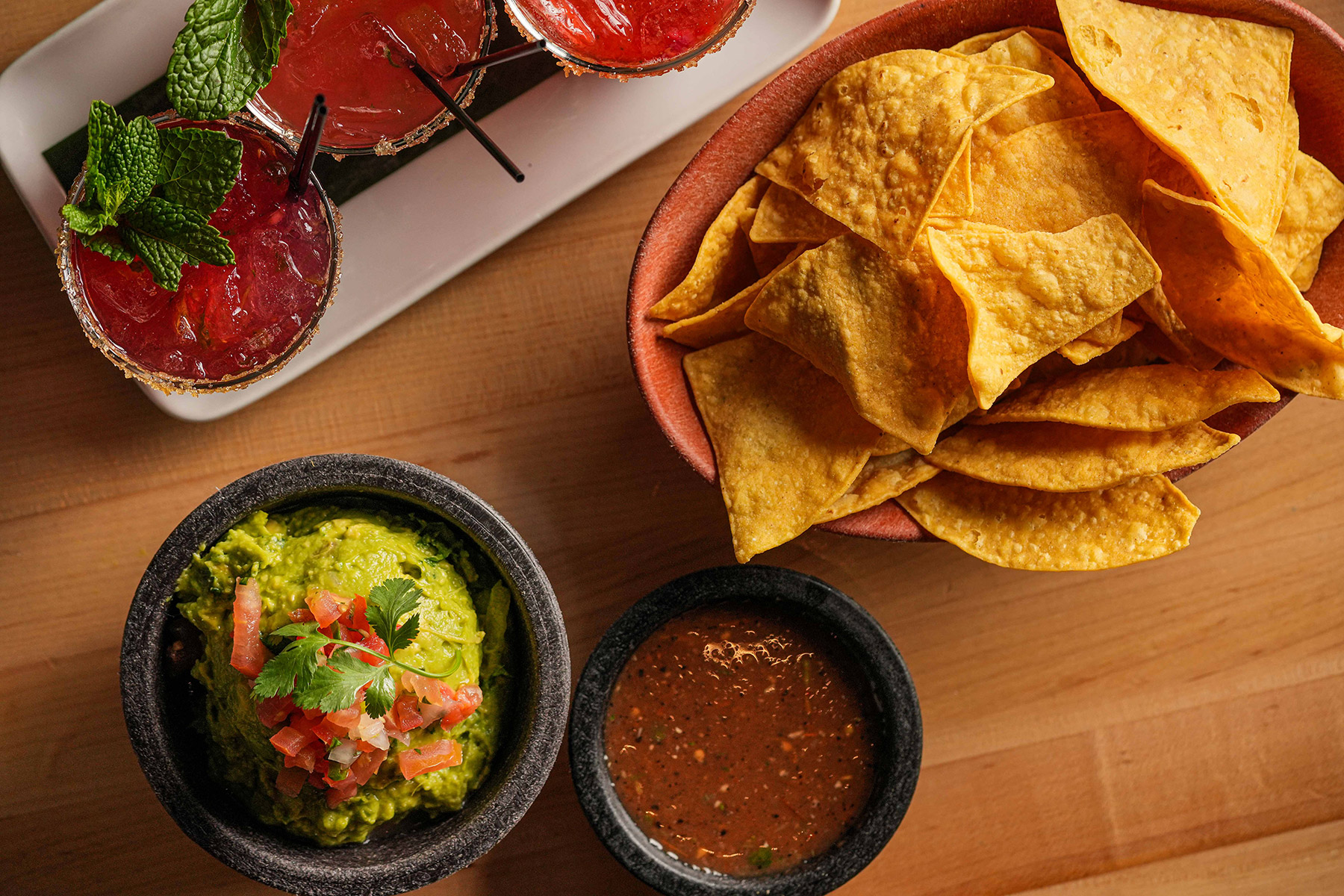 Tortilla chips served with fresh guacamole, salsa, and red cocktails garnished with mint.
