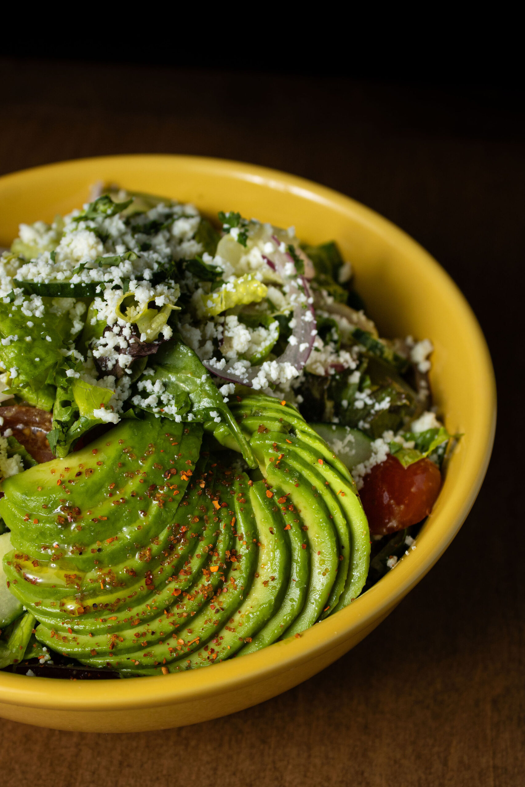 Fresh avocado salad with mixed greens, red onion, tomatoes, crumbled cheese, and sliced avocado.