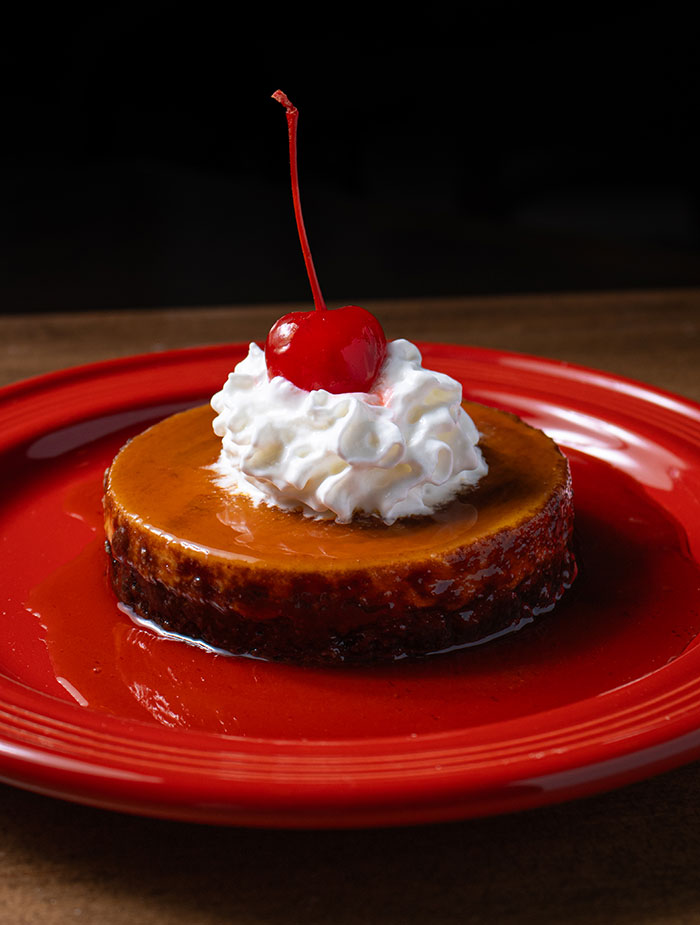Caramel flan topped with whipped cream and a maraschino cherry.